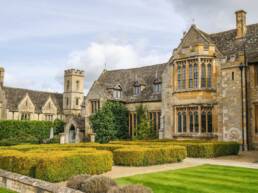 A view of the exterior of Ellenborough Park, a rustic building featuring impressive brickwork behind hedges and freshly-cut grass.