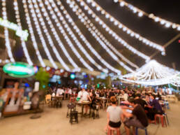 A view of people eating food at an outdoor street bar in Asia, lit up by many chains of fairy lights.