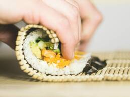 Sushi in the process of being rolled up by a pair of hands as part of GOTO Creates Sushi Making.