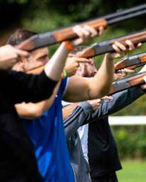 Four people lined up outdoors aiming shotguns upwards, as part of GOTO Creates Team Experiences.