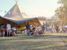 A blurred, defocused background of people in a park, enjoying a summer fair with marquees and bunting.