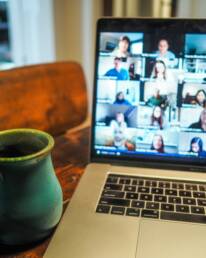 A laptop screen showing a virtual event, next to a green mug of tea.