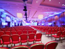 A conference hall with red chairs and coloured illumination as part of GOTO Creates AV Set-up.