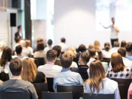 A speaker is giving a talk in a conference hall at a business event.