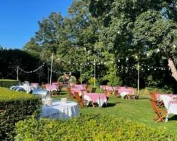 Outdoors picnic tables and chairs in a sunny garden area with fairy lights hung up.