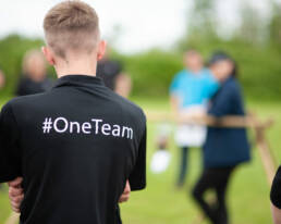 A view of the back of a mans black polo shirt, which reads #OneTeam, he is stood in a field delivering an event for GOTO Creates - Sherwoods One Team